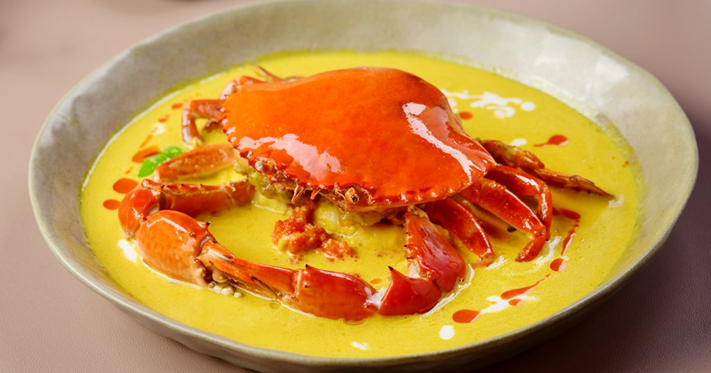 Whole crab in golden yellow curry sauce on a white plate