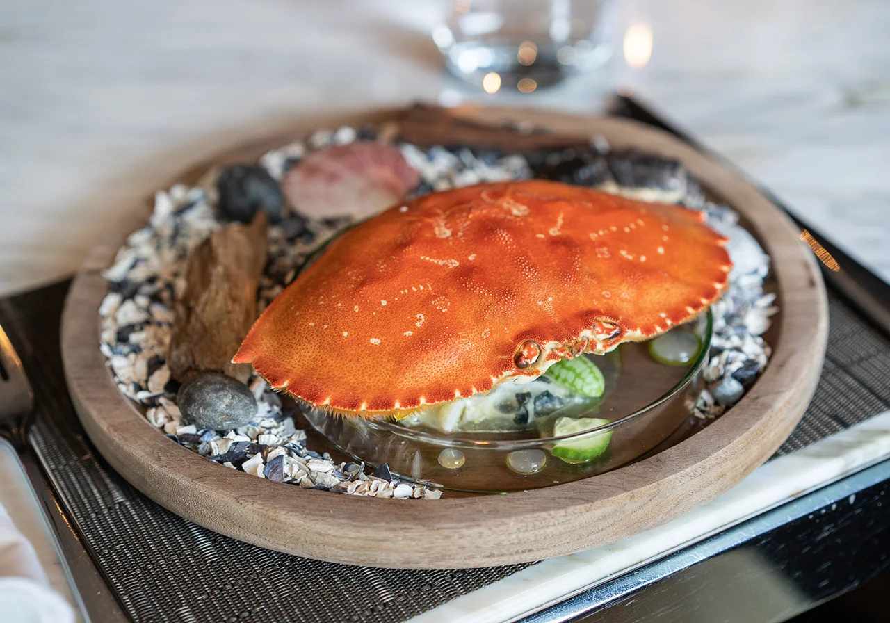 Whole crab served in a shallow broth bowl over stones